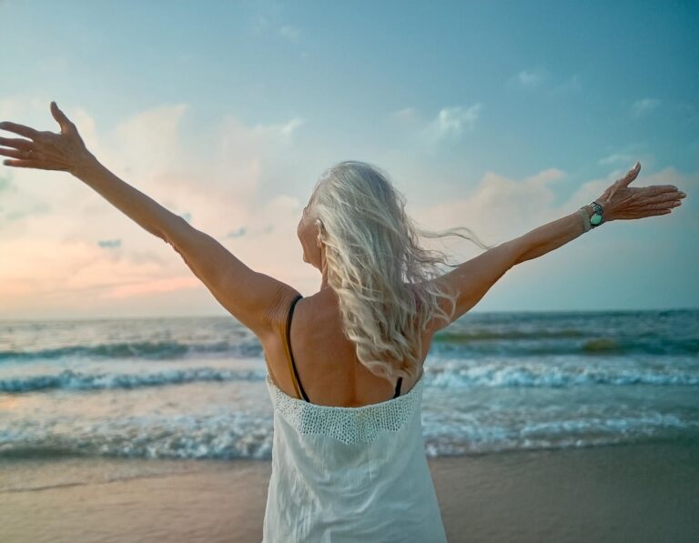 Lady arms open wide, enjoying life stood on a beach